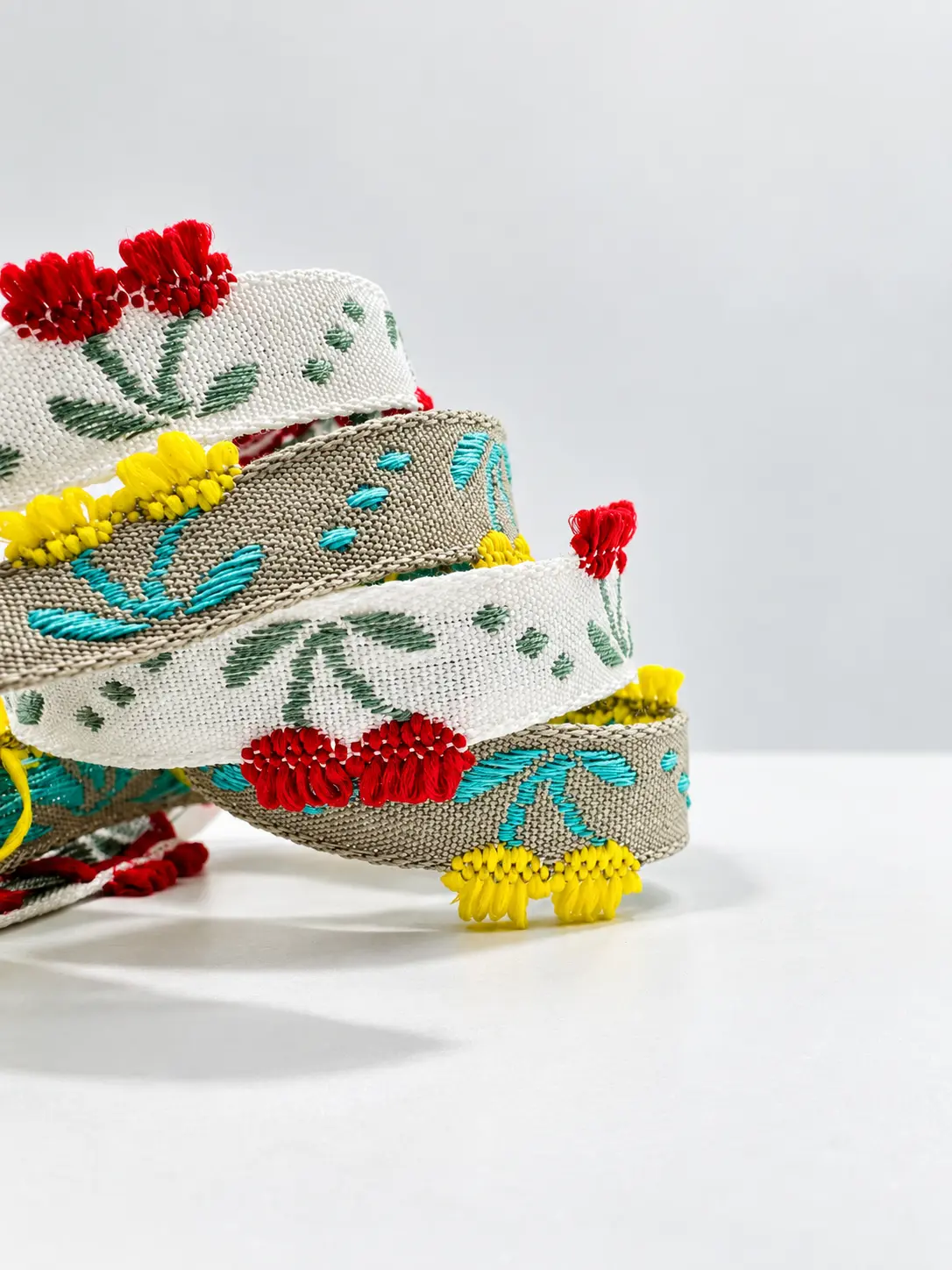 Galons jacquard écru et turquoise à motifs floraux, bordés de pompons rouges et jaunes — Maison Satab